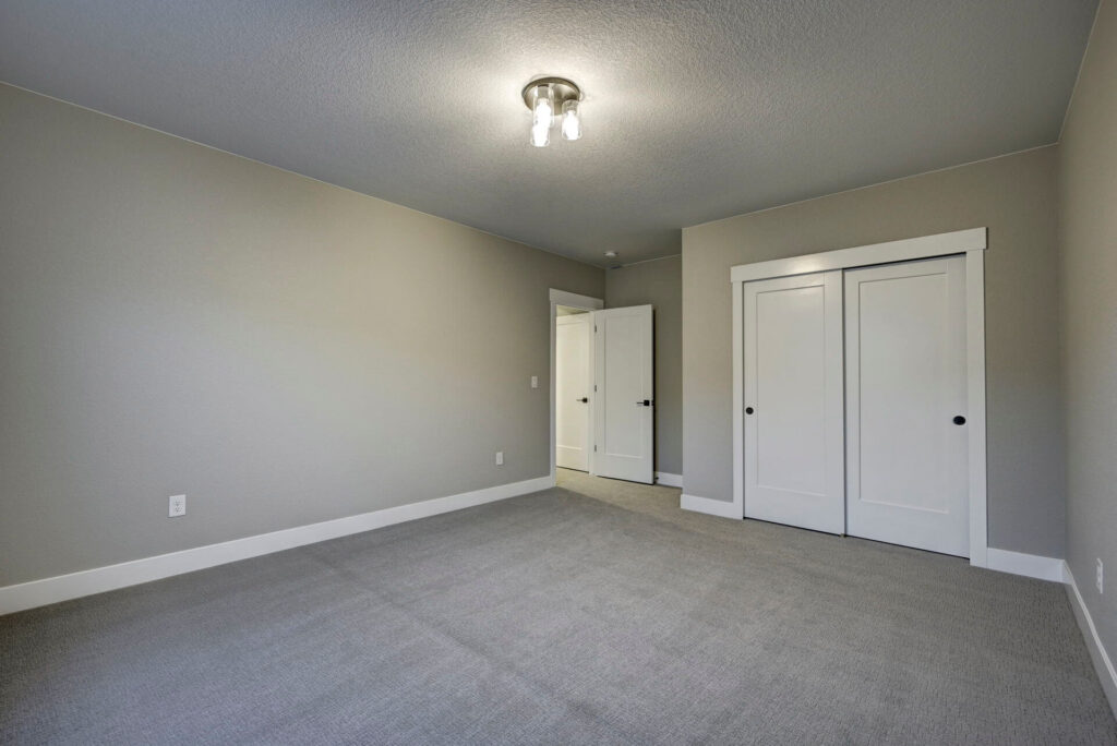 Spacious empty room with closet doors, carpet, and a ceiling light fixture.