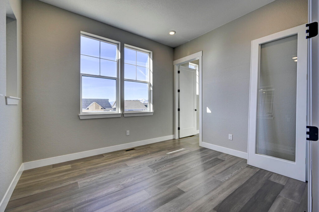 Bright empty room with two windows, light gray walls, and a glass-paneled interior door.