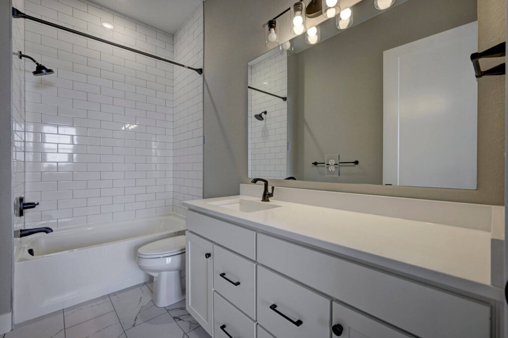 Bathroom with subway-tiled tub/shower, white vanity, and large mirror above sink.