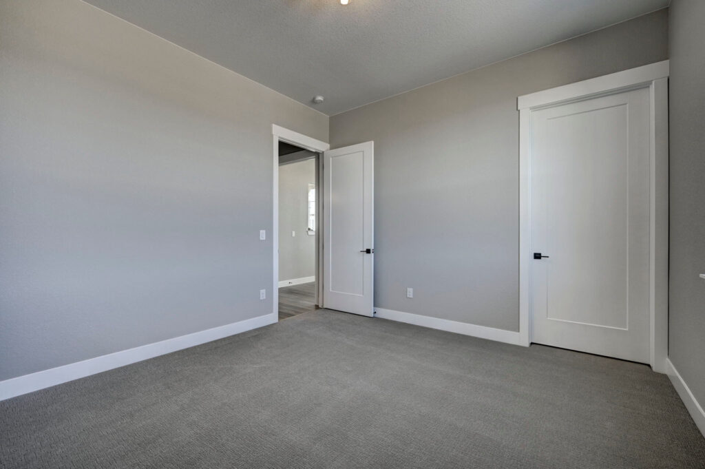 Empty bedroom with closed closet door and open entry door, gray walls and carpet.
