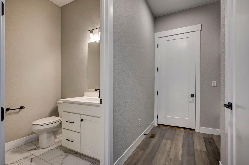 Small bathroom and adjacent hallway with white vanity, toilet, and mixed flooring.
