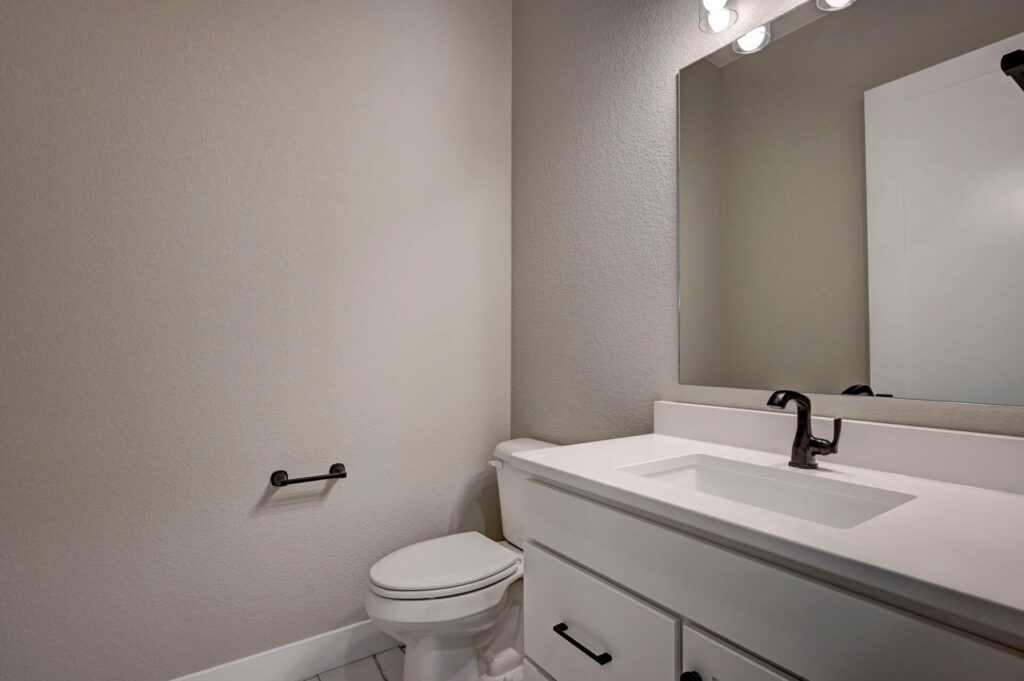 Powder room with single sink vanity, mirror, toilet, and neutral-tone walls.
