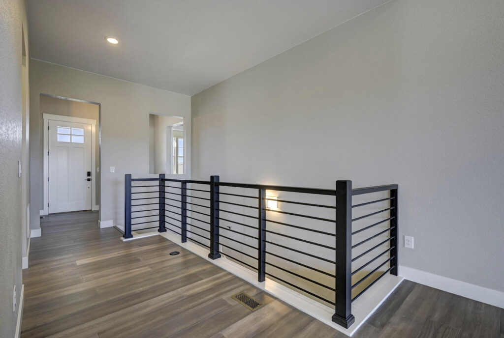 Upper hallway landing with horizontal metal railing and wood-look flooring.