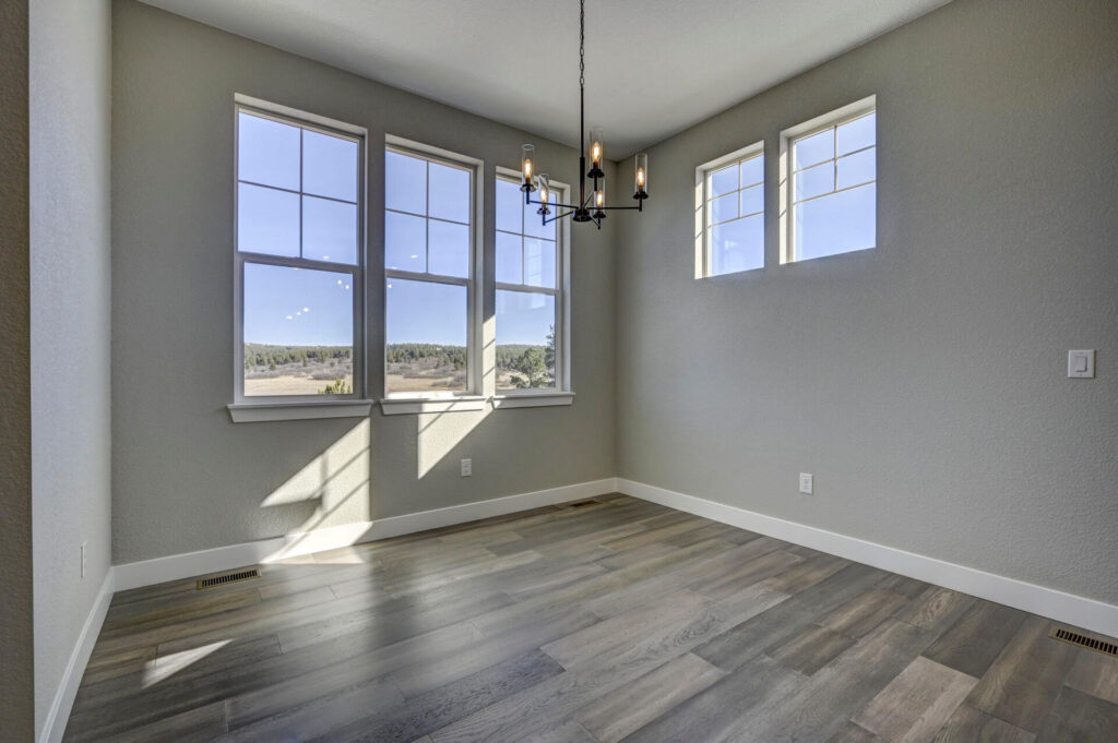 Empty dining nook with three large windows, a chandelier, and light gray walls.