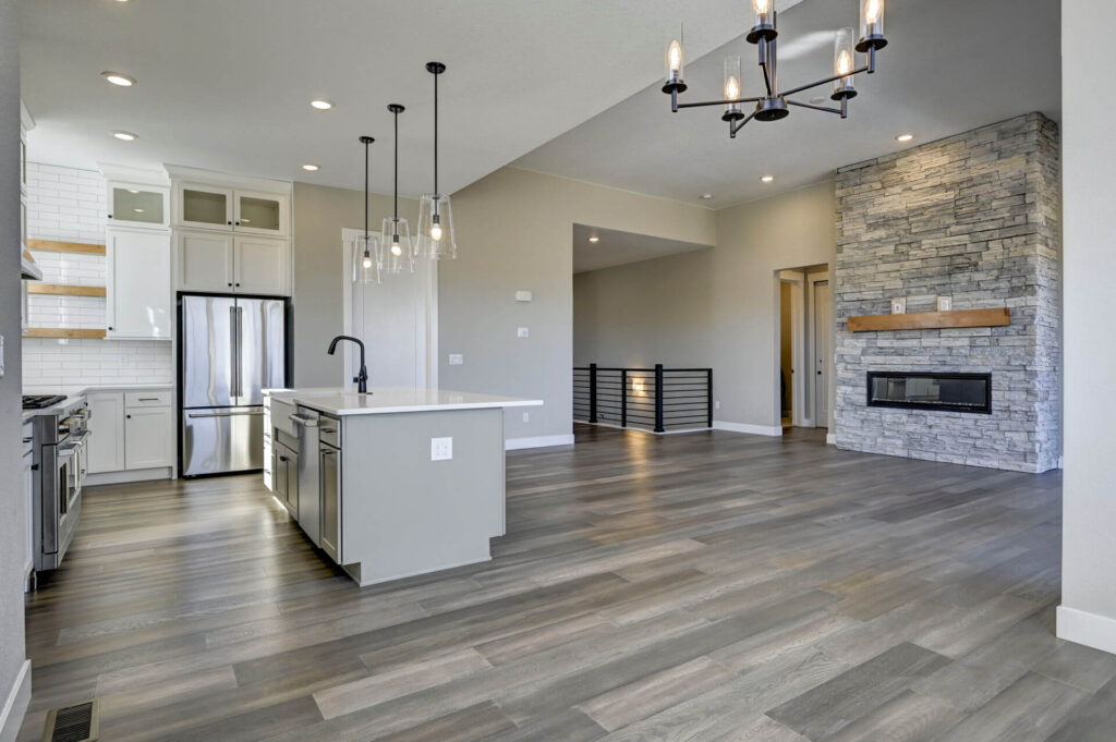 Wide view of kitchen and living room with island, stainless appliances, and stone fireplace.