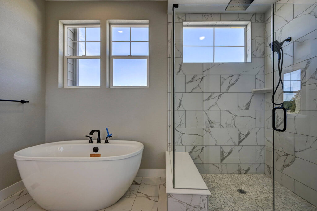 Freestanding bathtub beside a tiled walk-in shower with glass partition and transom windows.