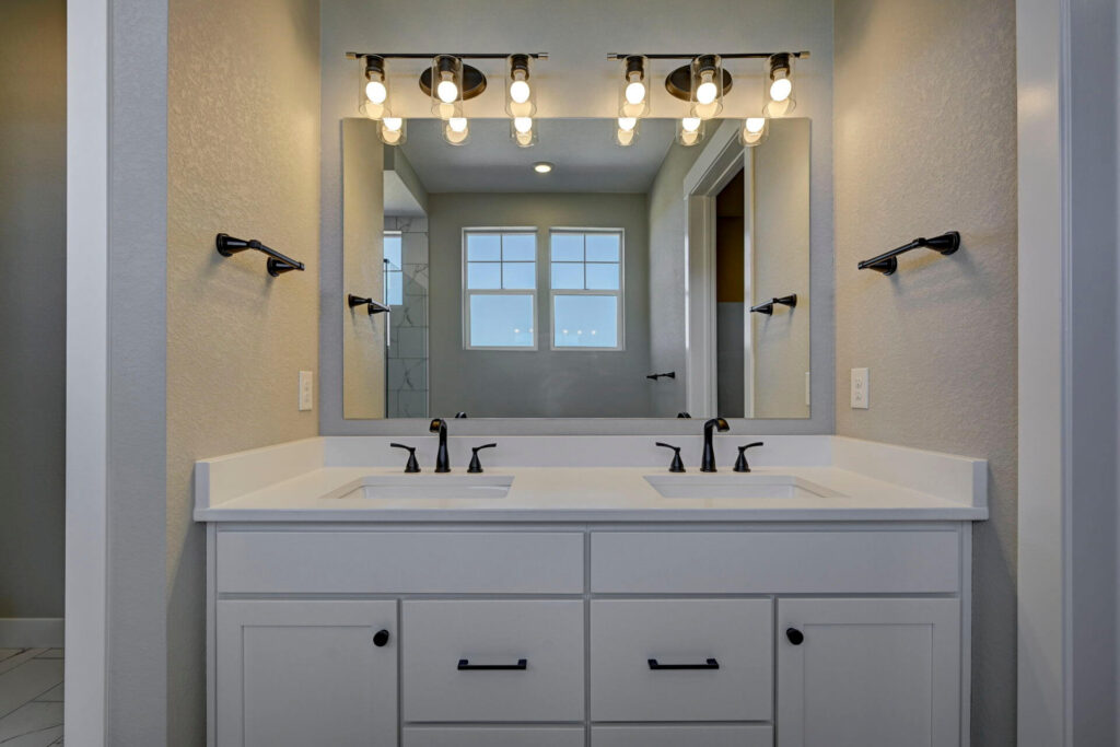 Double-sink vanity beneath a large mirror with exposed-bulb vanity lights and towel hooks.