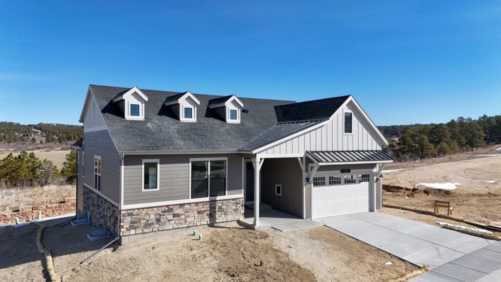 Angled front-left view of a farmhouse-style home with stone accents and a metal awning over the garage.