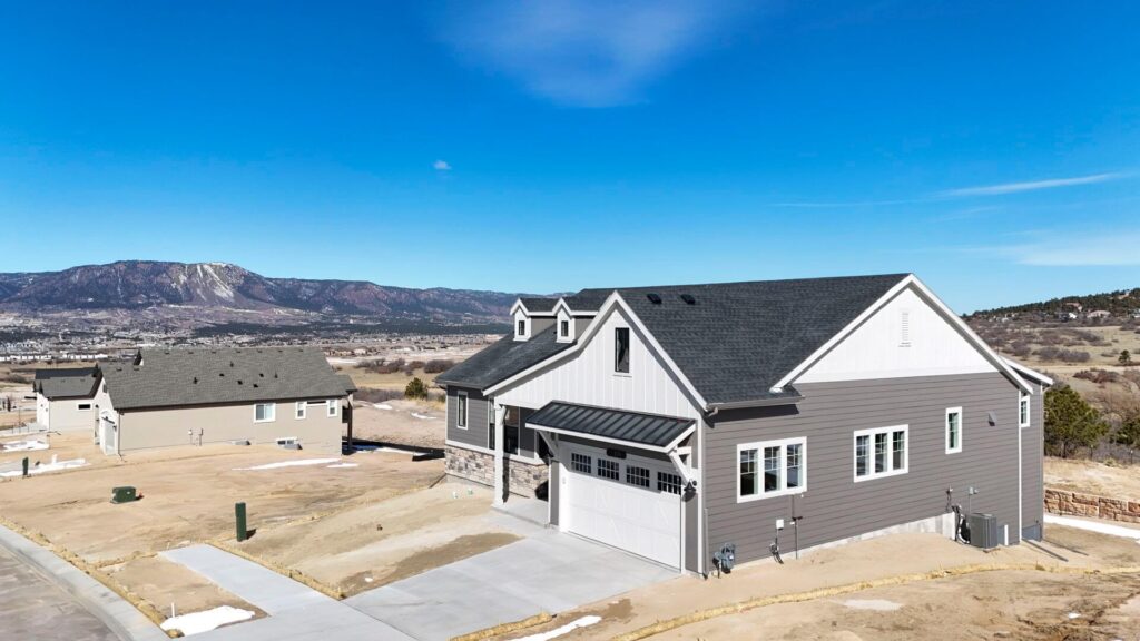 Aerial view of a newly built farmhouse-style home and neighboring lot with distant mountains.