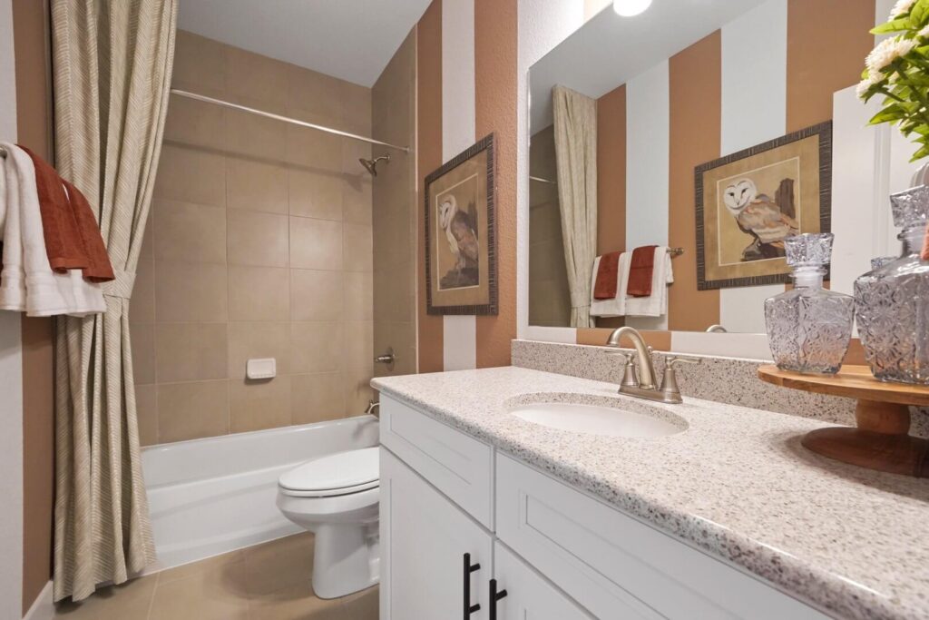 Bathroom with tub/shower, vanity with quartz countertop and striped wallpaper reflected in the mirror.