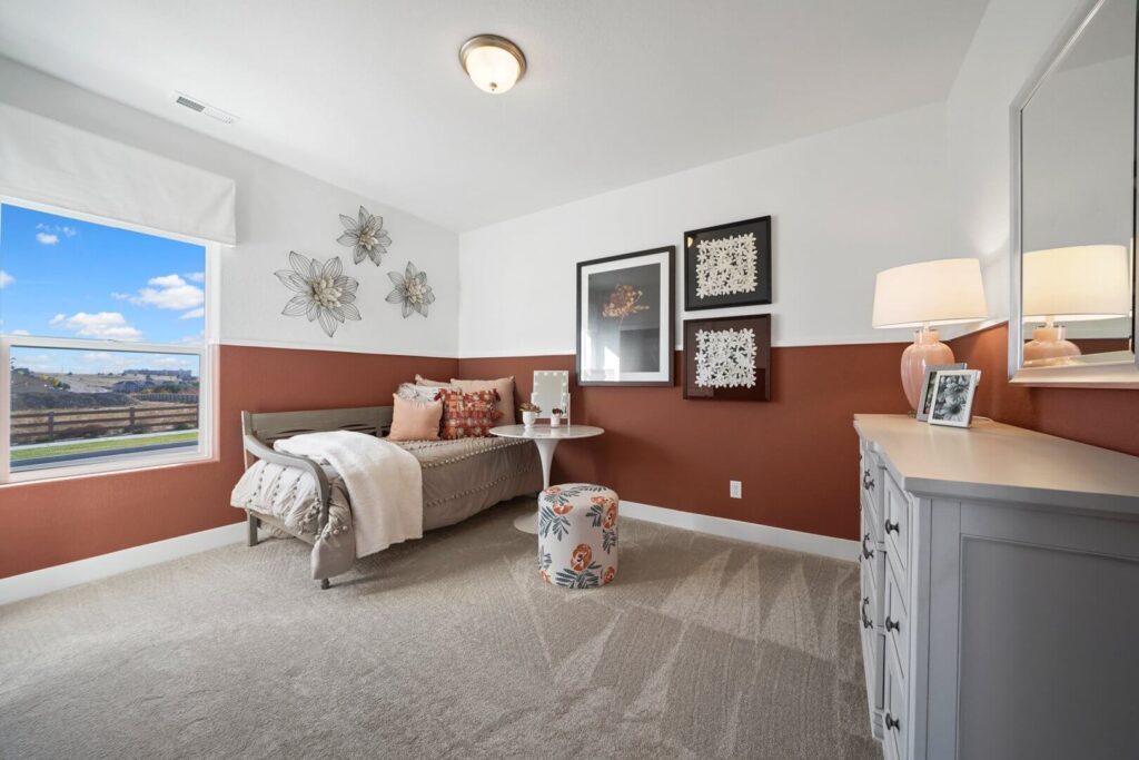 Staged bedroom with rust-colored lower walls, single bed, and floral ottoman by a window.