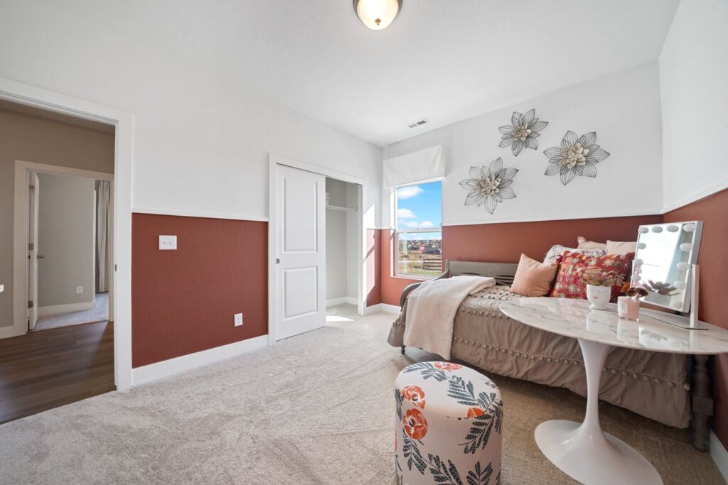 Corner view of a bedroom with an open closet, bed, and patterned ottoman near a window.