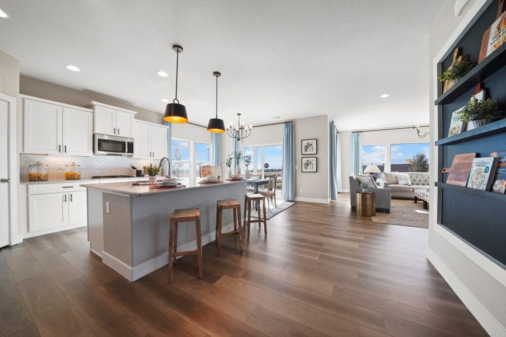 Open-plan kitchen and living area with island, three stools, pendant lights, and wide plank flooring.