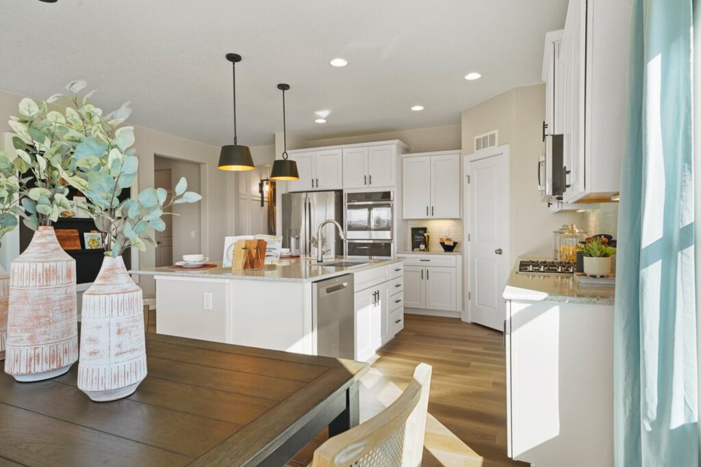 View from dining table toward kitchen island, pendant lights, and a sliding-windowed dining area.