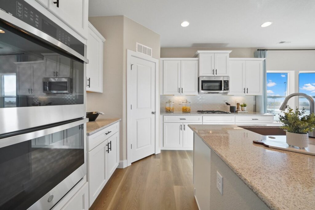 Kitchen counter and appliances with built-in oven, microwave, pantry door, and quartz island countertop.