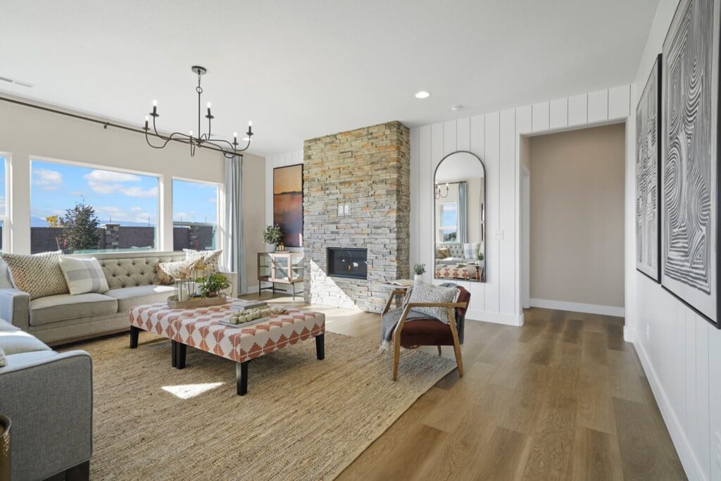Sunlit living room with large windows, stone fireplace, and mixed-seating arrangement on wood floors.