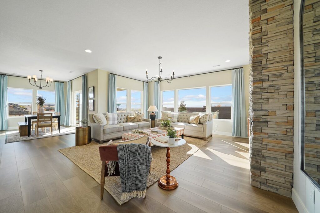 Open-plan living and dining area with multiple windows, sofas, and a stone column near the seating.
