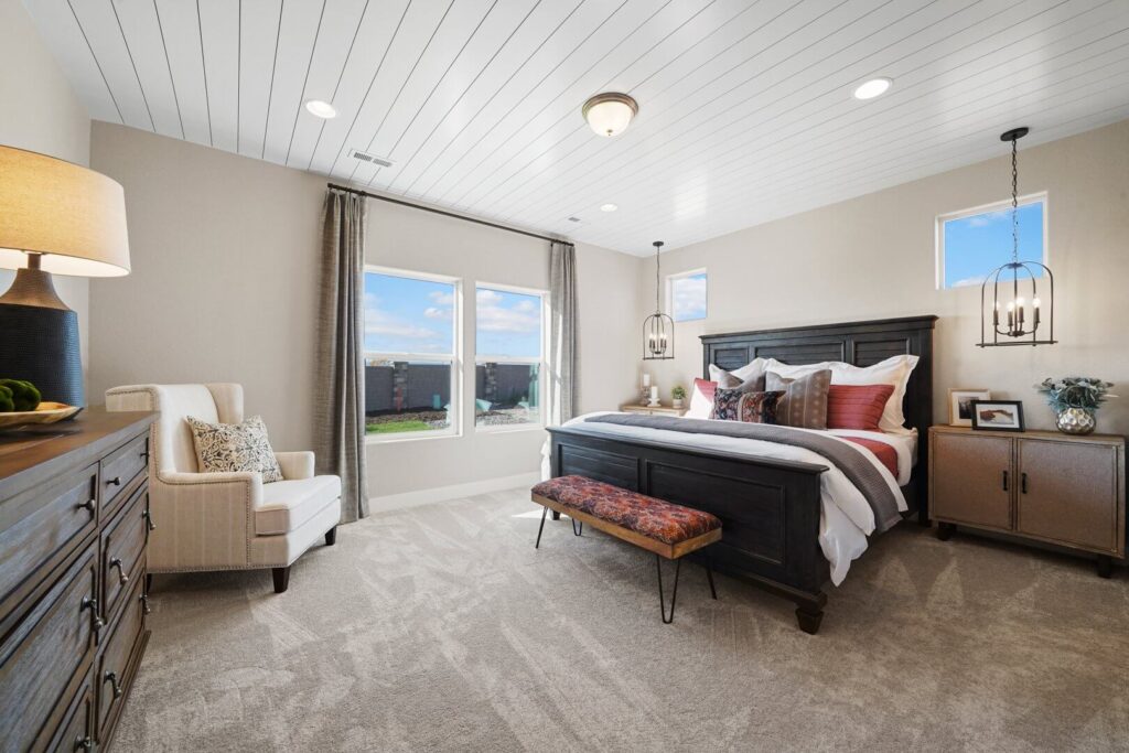Bright bedroom with dark wooden bed, upholstered chair, and large windows overlooking outdoors.