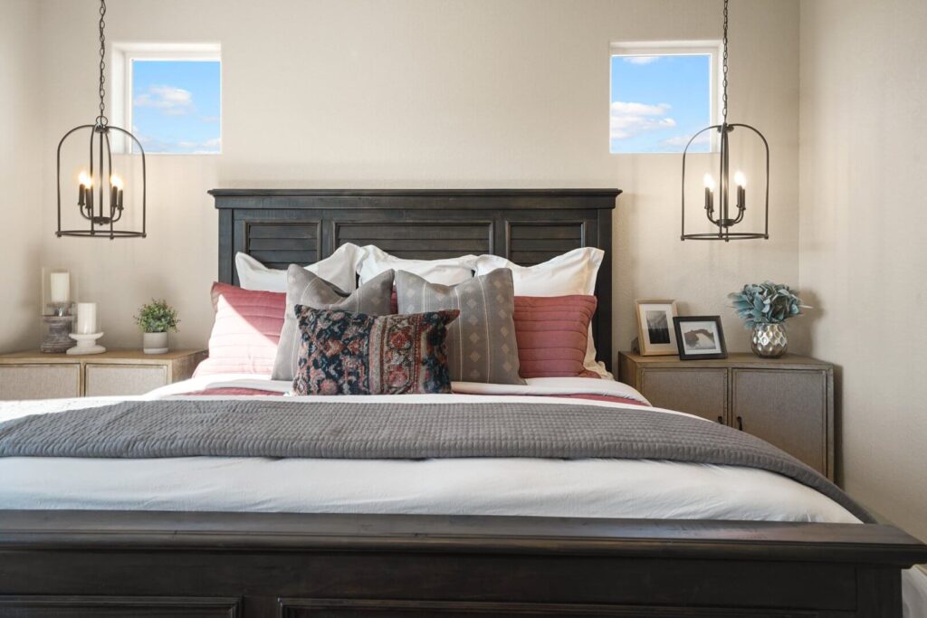 Close-up of a made bed with multiple decorative pillows, dark headboard, and pendant lights at each side.