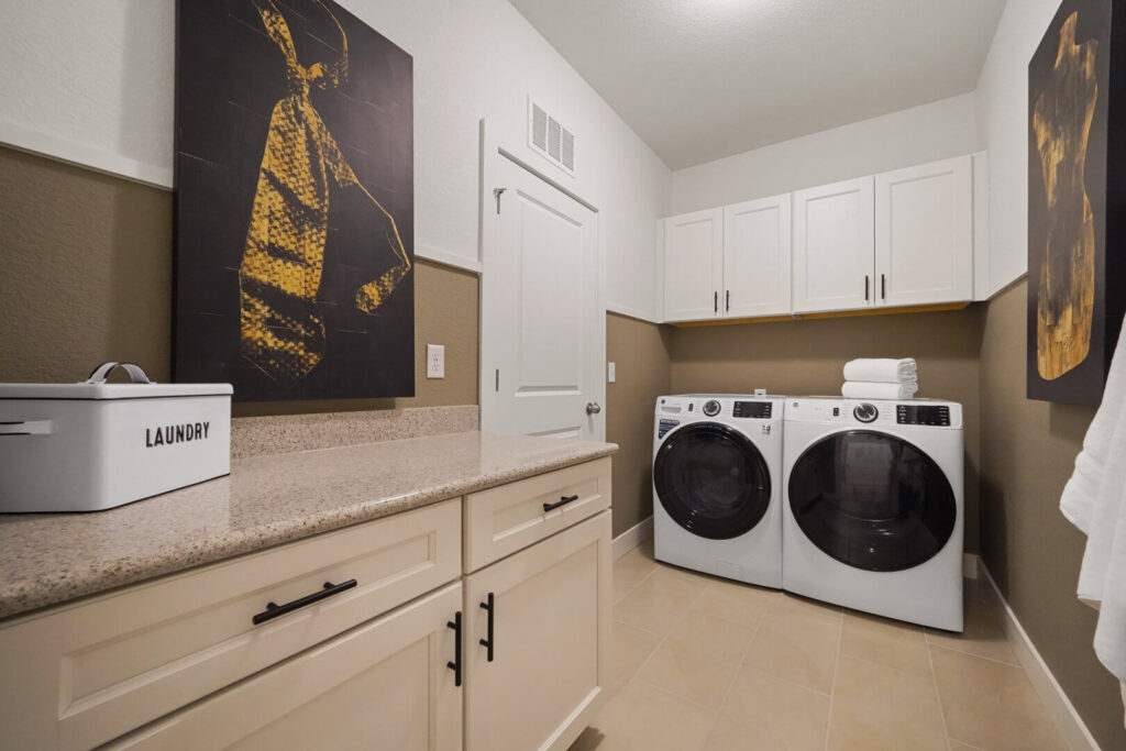 Laundry room with countertop, lower cabinets, washer and dryer, and two large framed artworks.