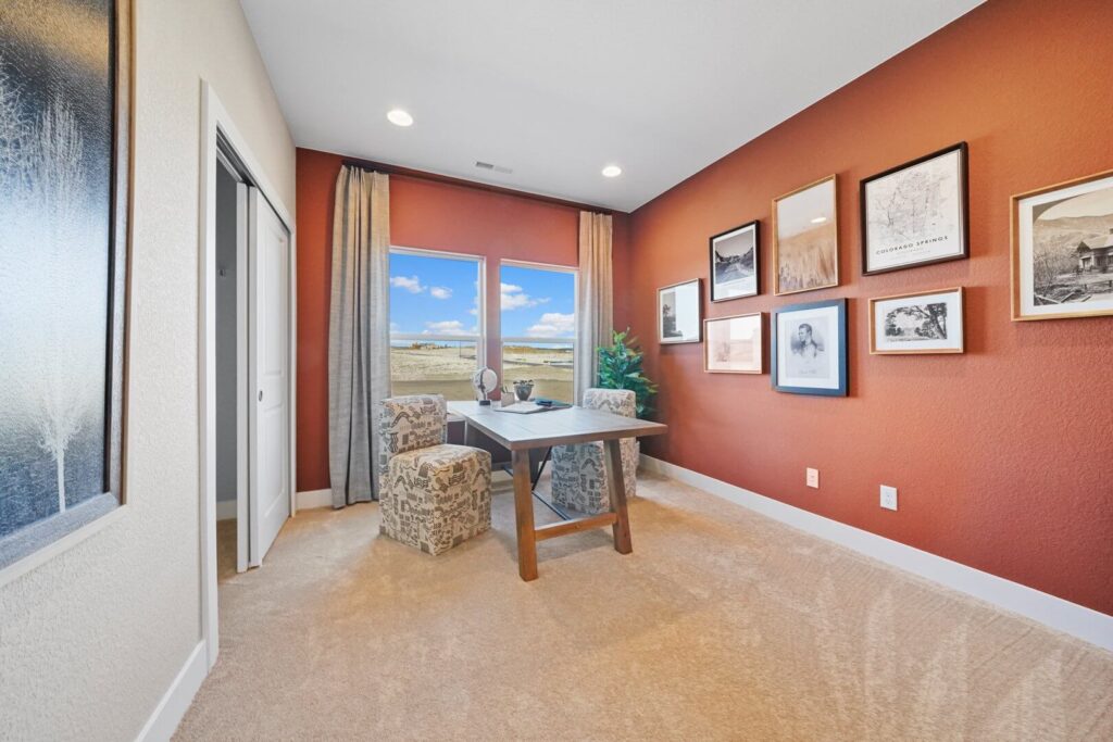 Home office with a table, two patterned chairs, red accent wall, and window with drapes.