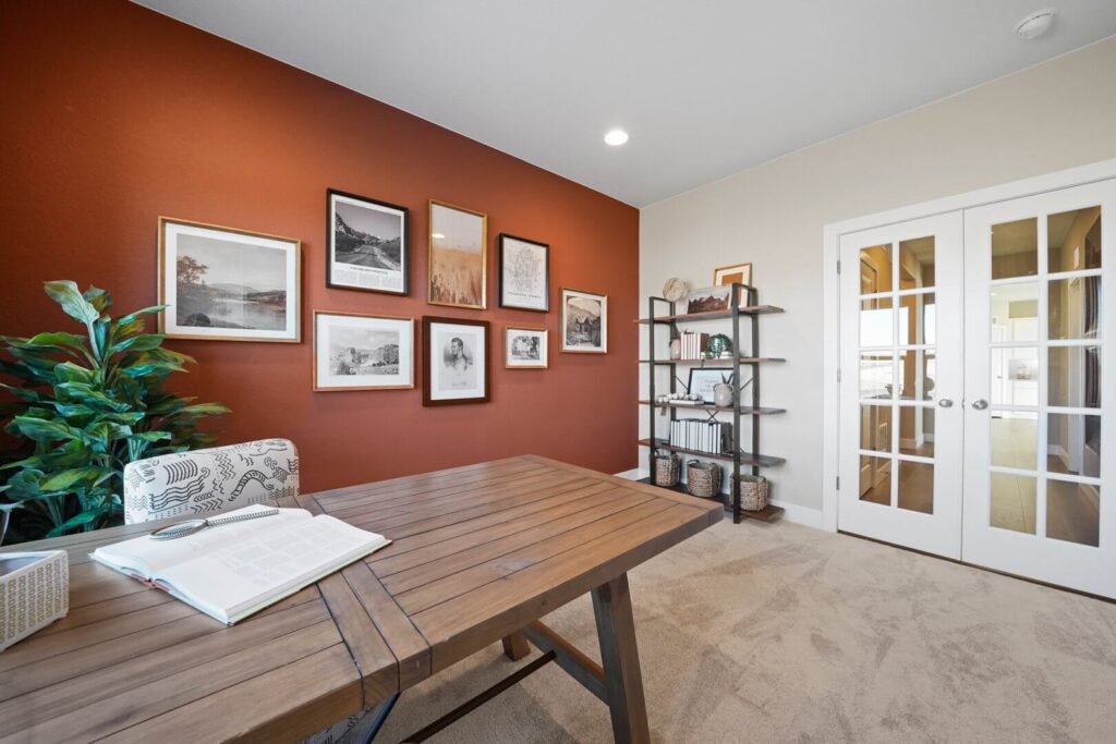 Office space with wooden desk, gallery wall on red accent, shelving unit, and French doors.