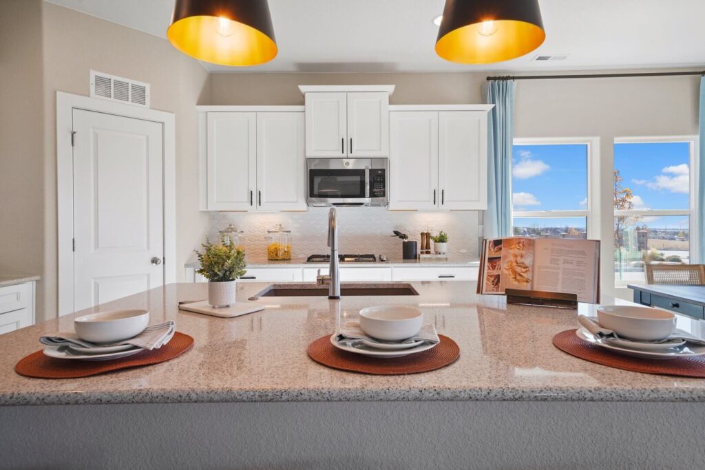 Bright kitchen island with place settings, pendant lights, and a view to windows and white cabinets.