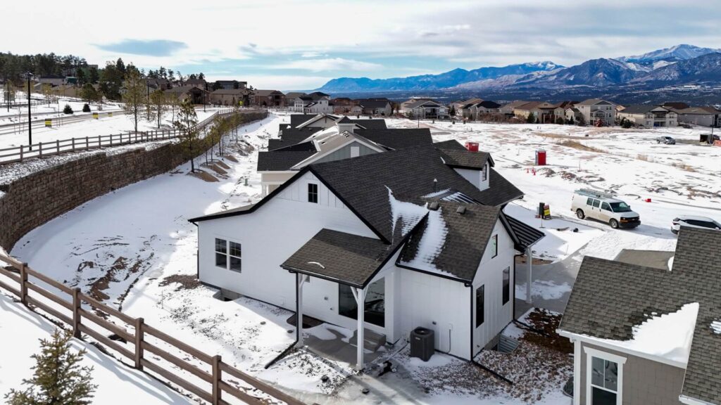 Aerial view of several white houses in a snowy neighborhood with mountains in the distance.