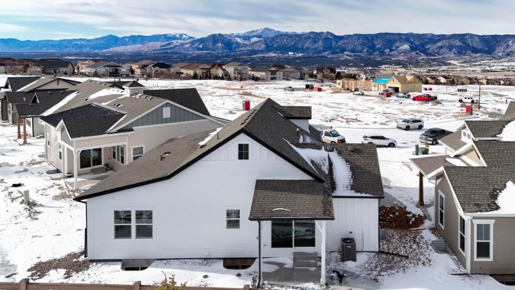 Aerial rear view of a row of houses on a snowy lot with mountains visible in the background.