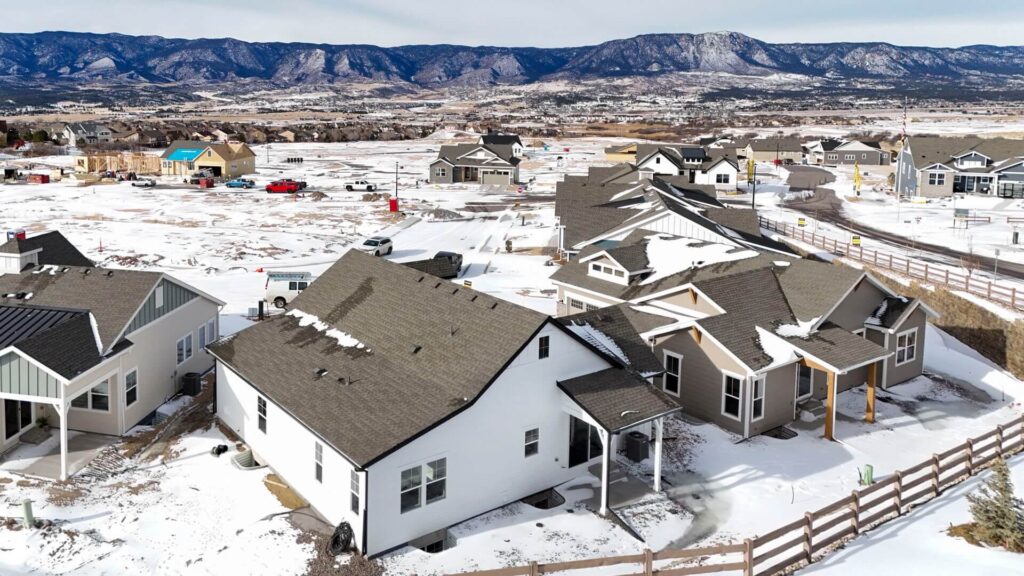 Oblique aerial view of a residential development with several houses and snowy streets near distant mountains.