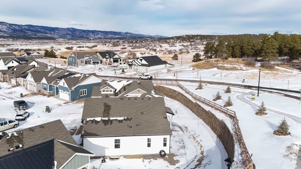 Aerial view of a snowy suburban neighborhood with houses, roads, and distant hills.