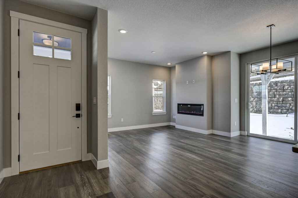 Empty living area with entry door, wood-look floors, wall-mounted linear fireplace, and sliding glass door.
