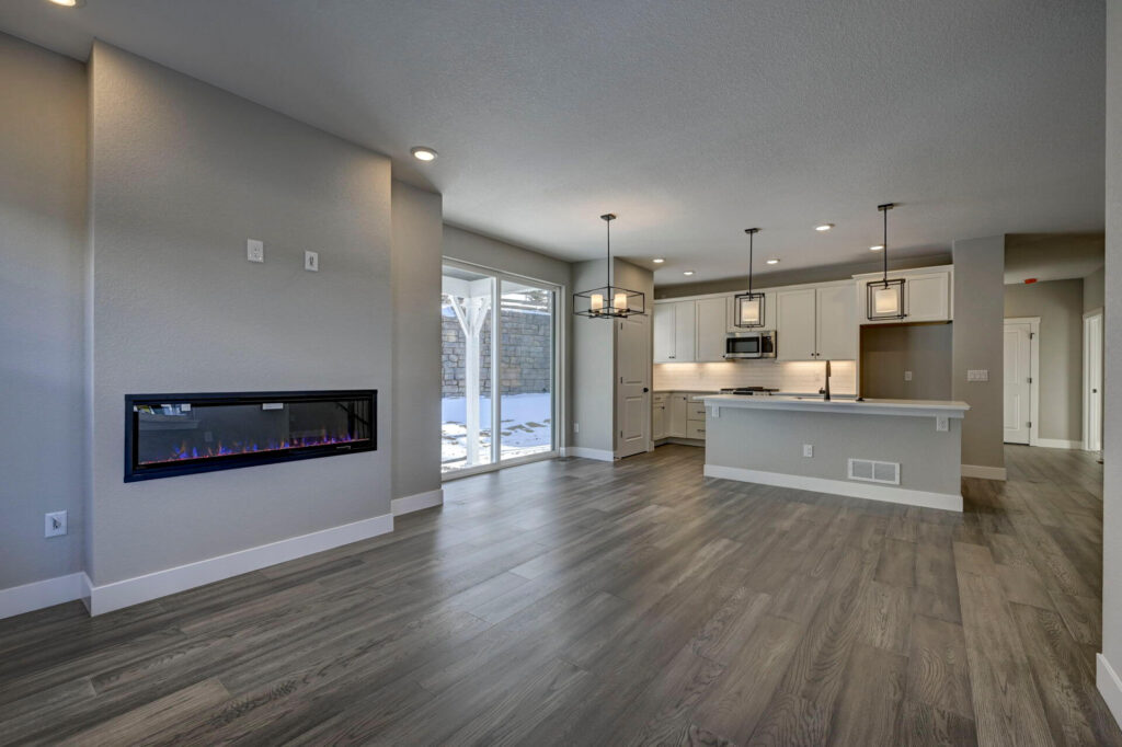 Living area with linear wall-mounted fireplace and open kitchen beyond, sliding glass door to yard.
