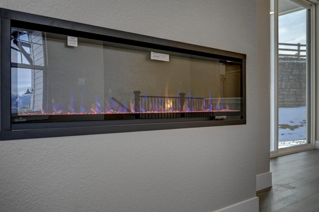Long recessed linear gas fireplace with blue flames set into a light textured wall.