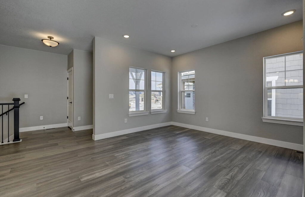 Empty light-filled living area with gray walls, three windows, and wood-look flooring.