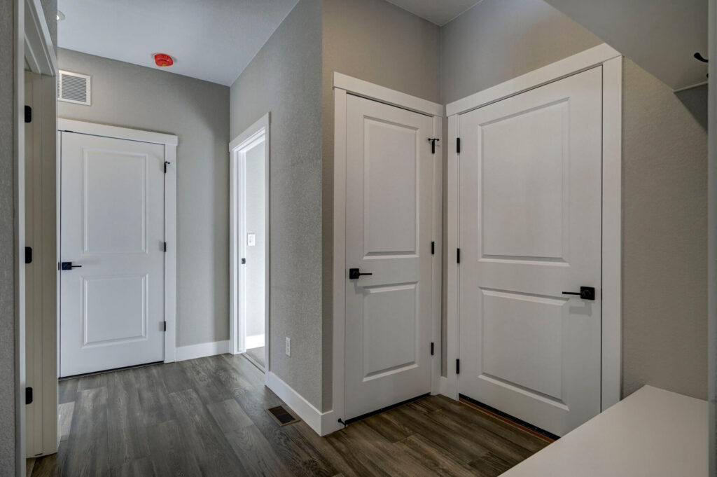 Interior entryway with three white doors, gray walls, and wood-look flooring.