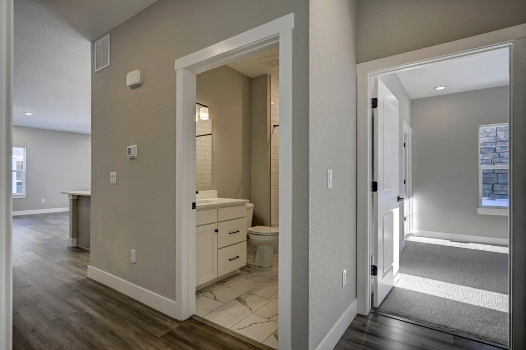 Open doorway to a tiled bathroom and a carpeted room, seen from a central hallway.