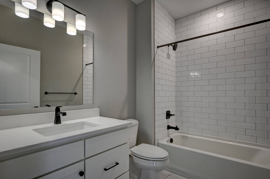 Bathroom with white vanity, toilet, and bathtub with white subway tile surround and dark fixtures.