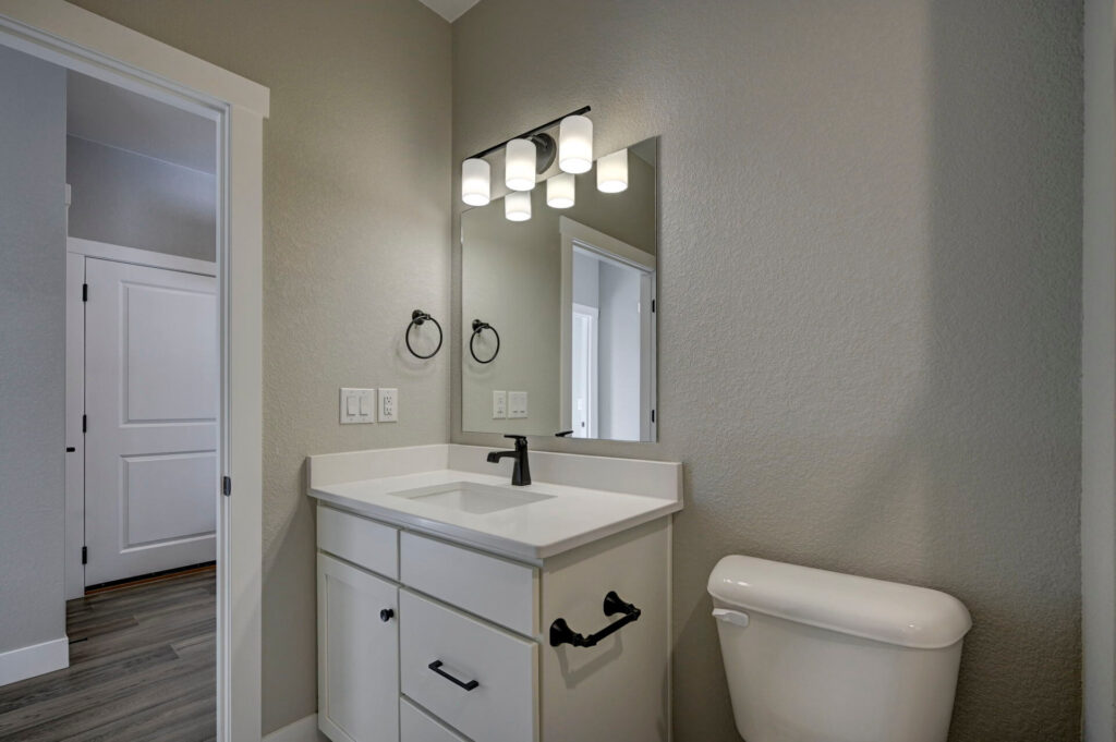 Small bathroom vanity area with mirror, three-light fixture, and a toilet beside the sink.