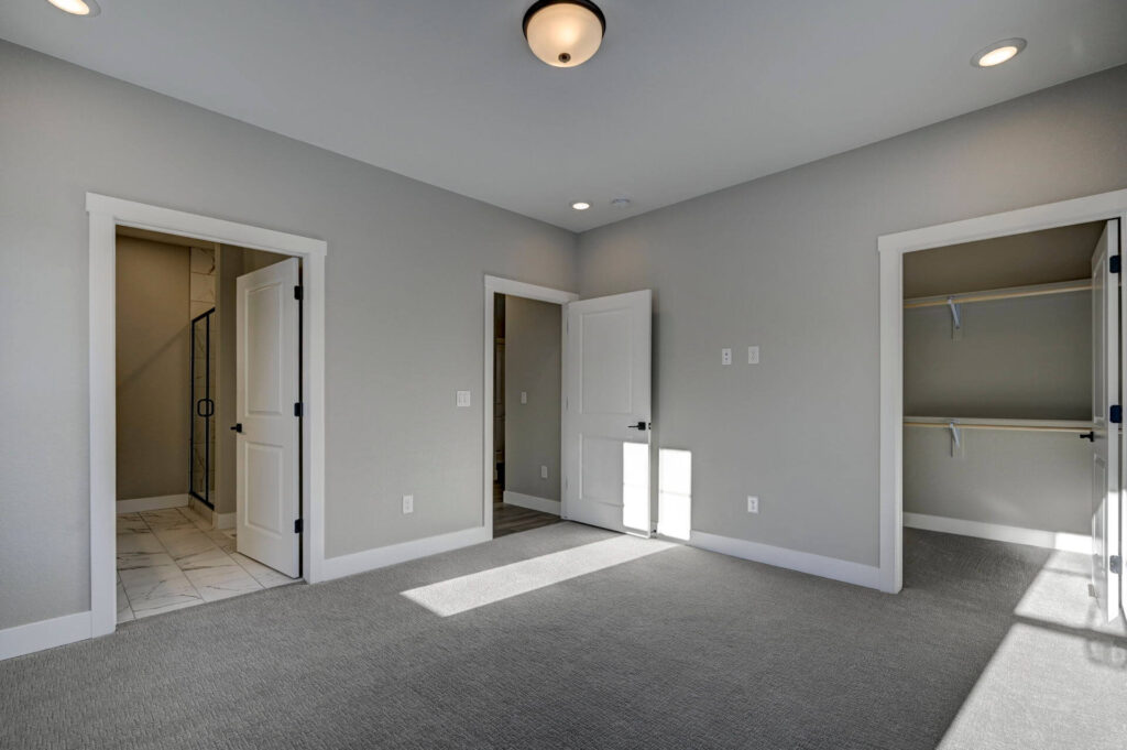 Empty carpeted bedroom with two open doorways and a walk-in closet visible to the right.