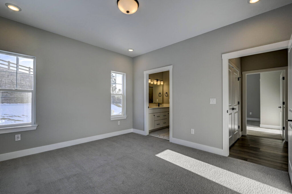Bright empty bedroom with two windows and an open doorway to an en-suite bathroom.