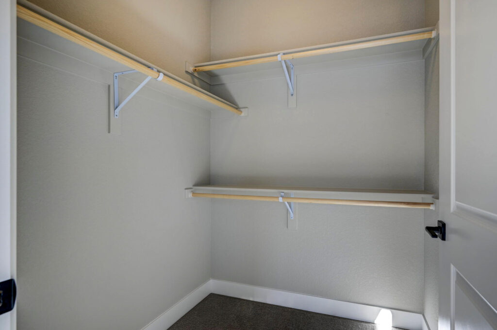 Small walk-in closet with multiple wooden hanging rods and white shelving supports.
