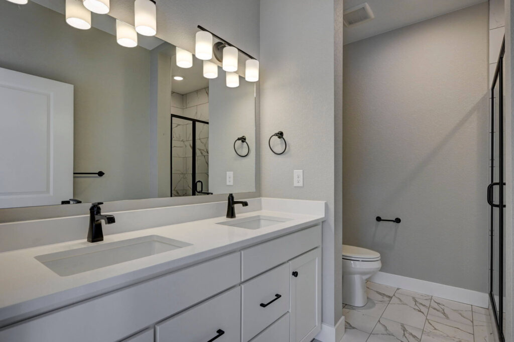 Bathroom vanity with dual sinks, large mirror, and a toilet in a separate alcove.