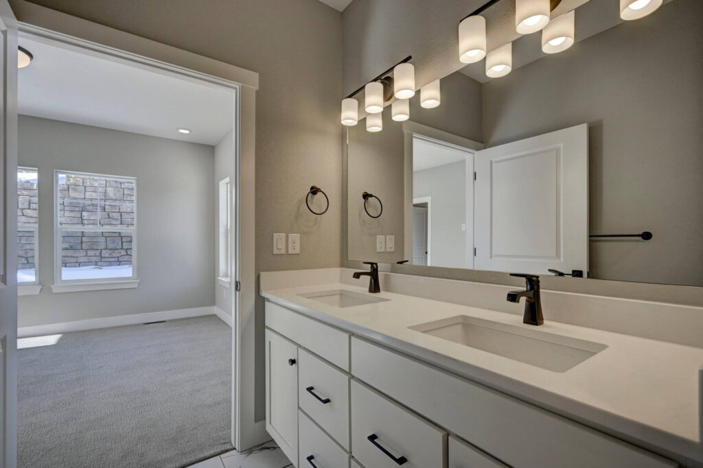 Double-sink vanity with large mirror and pendant-style lights, open door to adjacent room.