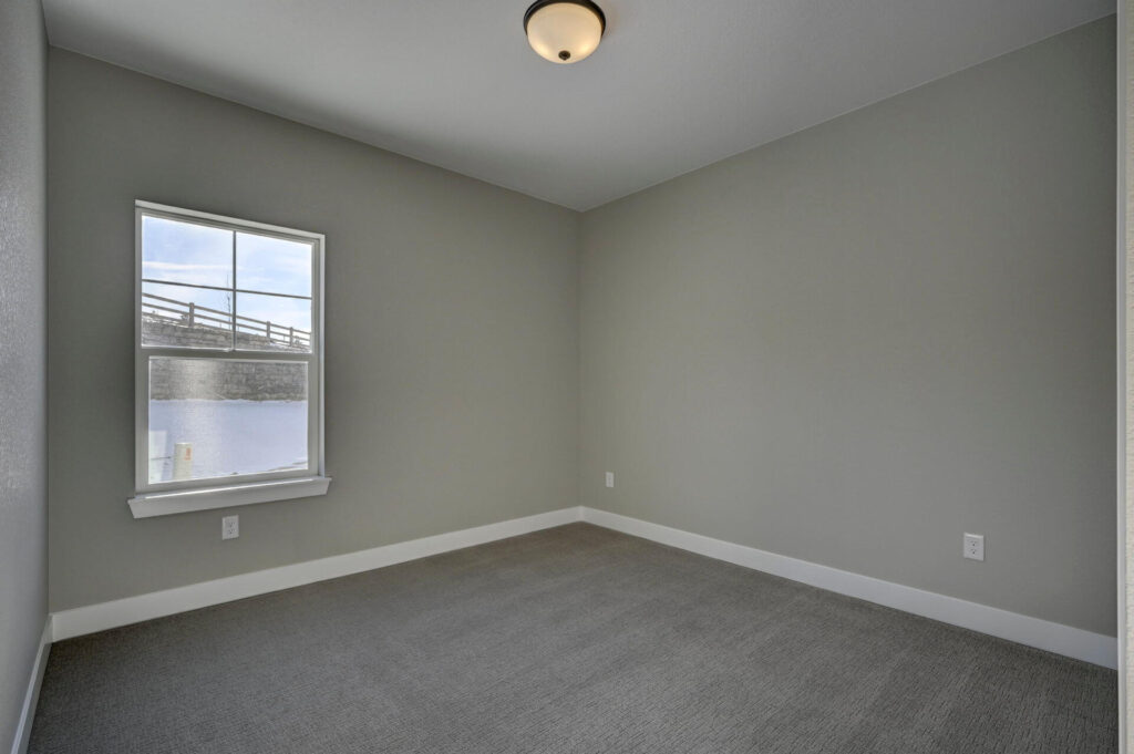Empty room with single window, gray walls, carpeted floor and ceiling light fixture.