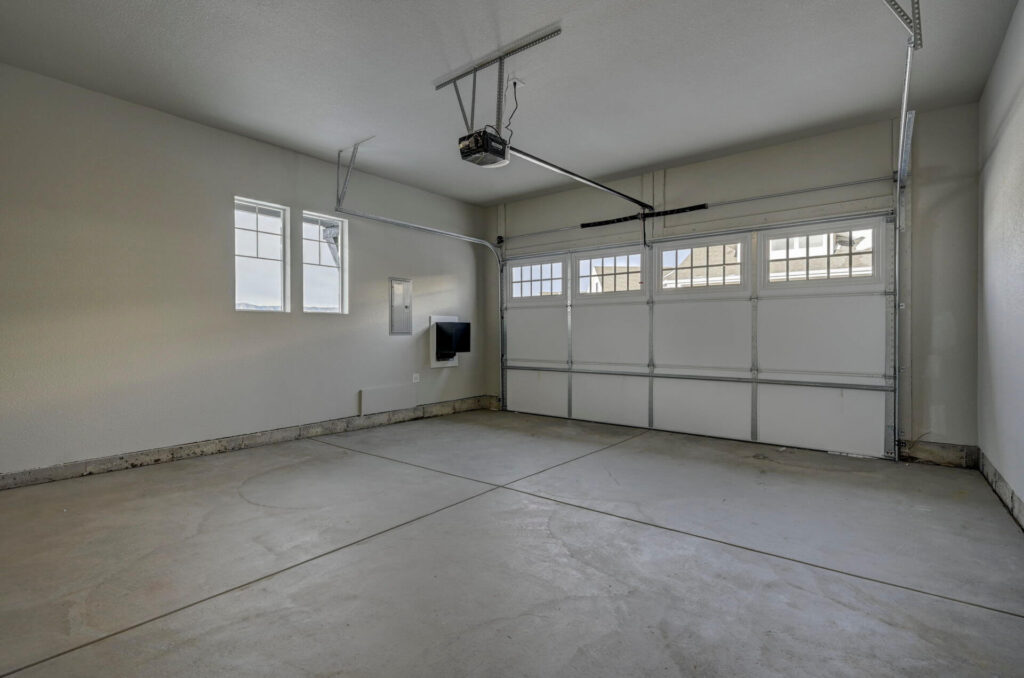 Two-car garage interior with concrete floor, overhead door and small side windows.
