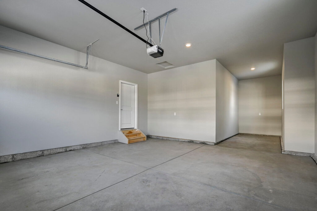 Interior garage view with entrance door, concrete floors and recessed lighting.