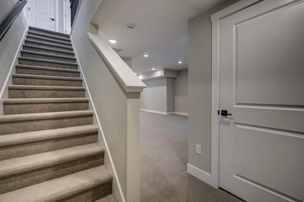 Carpeted staircase beside a finished lower-level hallway with closed door and recessed lights.