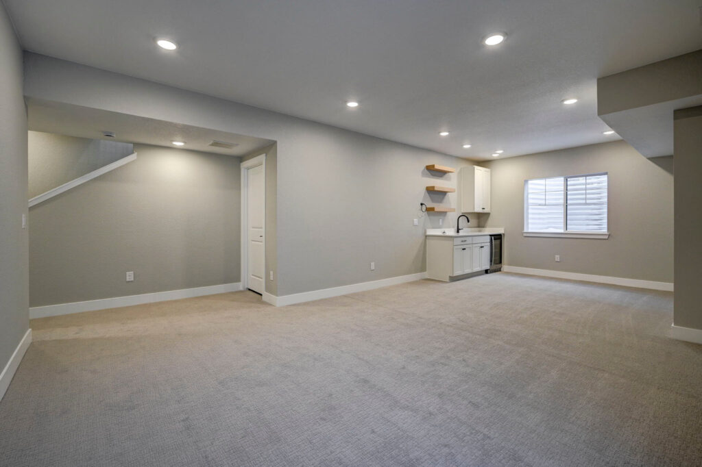 Expansive finished basement space with recessed lighting, mini kitchen, and window.