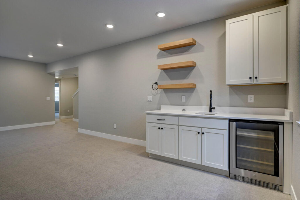 Long finished room view showing a wet bar with cabinets and shelves on the right and open floor space.